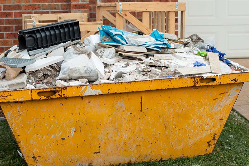 Yellow skip on garden lawn filled with waste