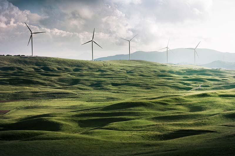 Wind turbines on a green hill with clouds in the sky