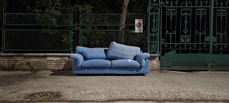A blue sofa fly-tipped on a pavement