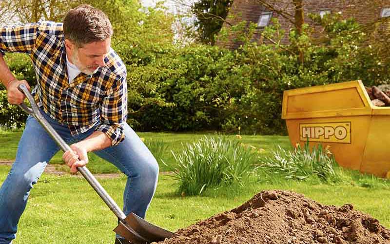 Man filling skip with soil in garden