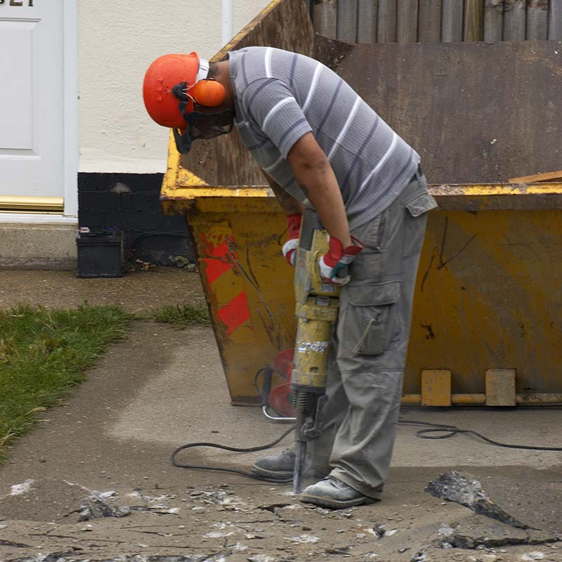 Workman drilling near a skip