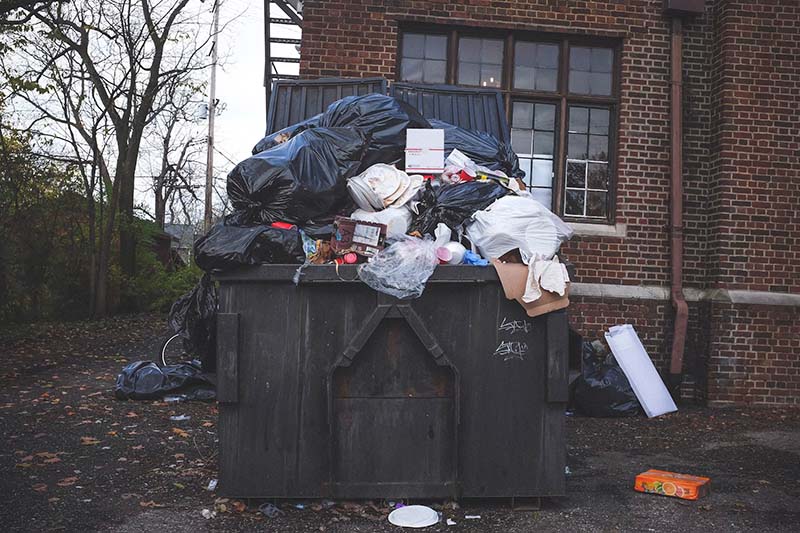 A business waste skip overfilled and overflowing causing littering outside