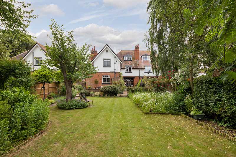 A lawn in the back garden of a house with flowerbeds and trees