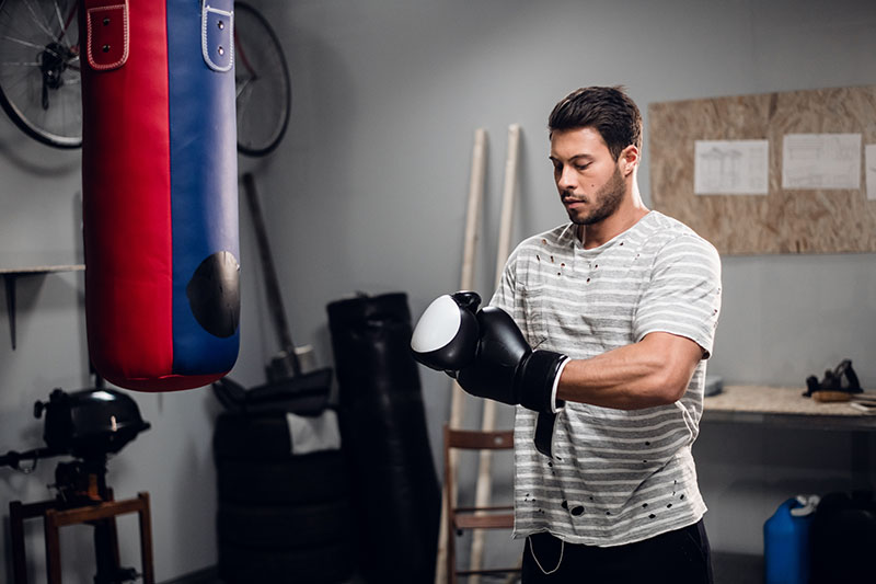 A man with boxing gloves and a punchbag hanging in a gym in a garage