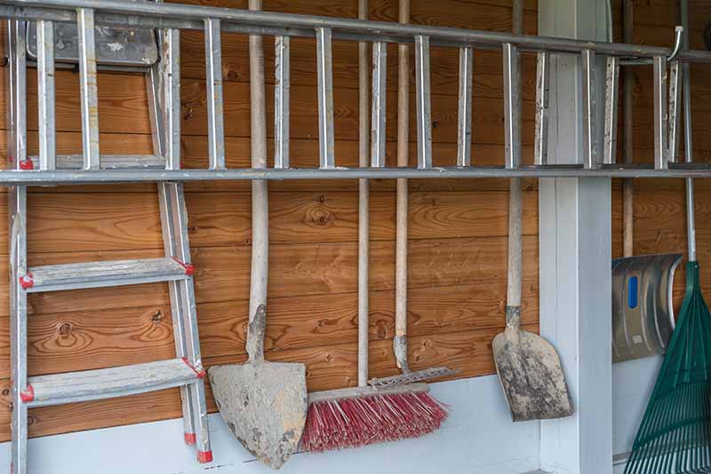 A tidy garage wall with garden tools and ladders hanging