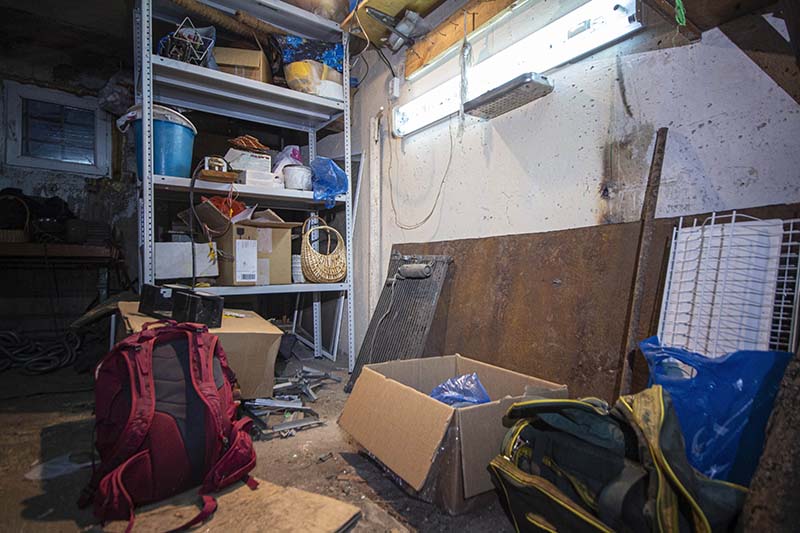 A messy garage with boxes, bags and clutter on the floor and racking full of items