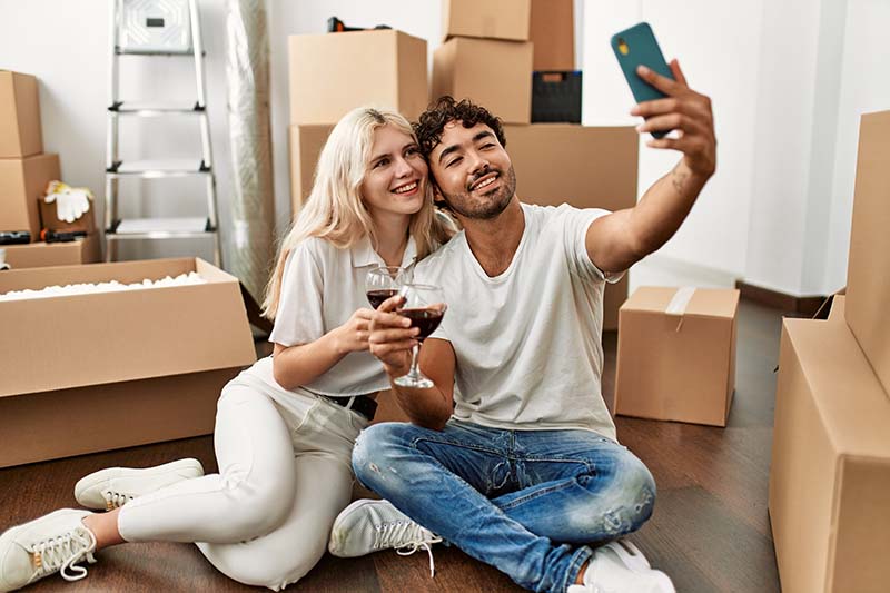 A couple taking a selfie holding wine glasses in their newly moved into home with packing boxes