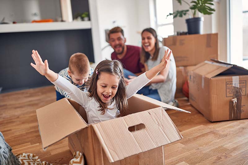 Girl and boy playing with an empty moving box with parents watching