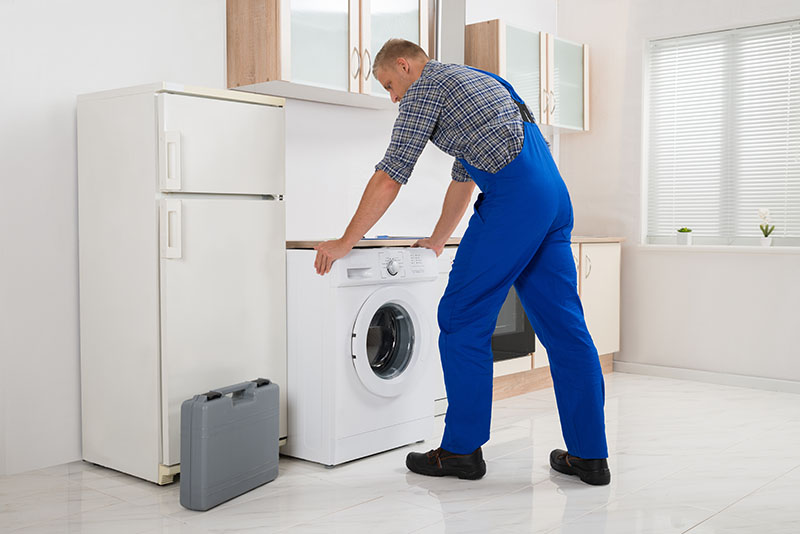 A person moving a washing machine from under a kitchen counter