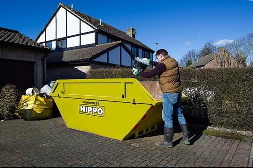 Man disposing waste into a skip on a driveway