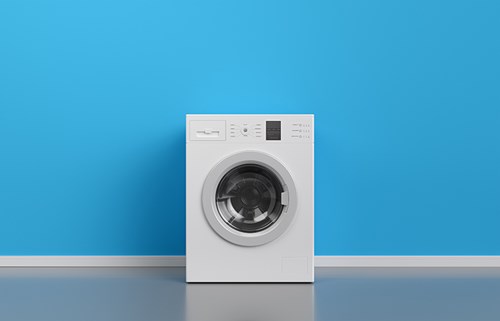 A washing machine placed on a floor against a blue wall