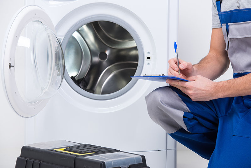 Person with a clipbaord knelt in front of a washing machine