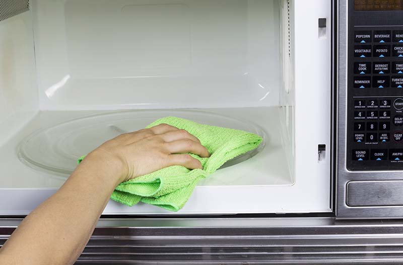 A person cleaning the inside of a microwave with a green microfibre cloth