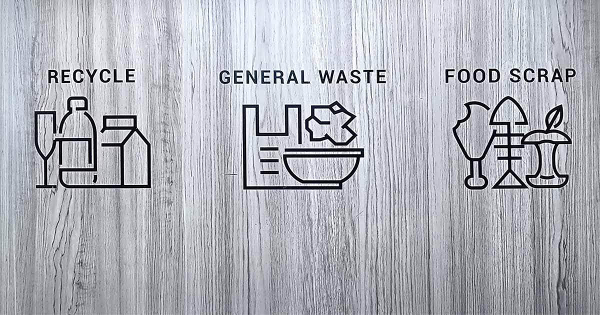 Simpler Recycling scheme icons for recycling, general waste and food waste on a grey wood background